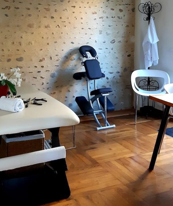Le cabinet : table de soin, chaise de massage et mur de pierre